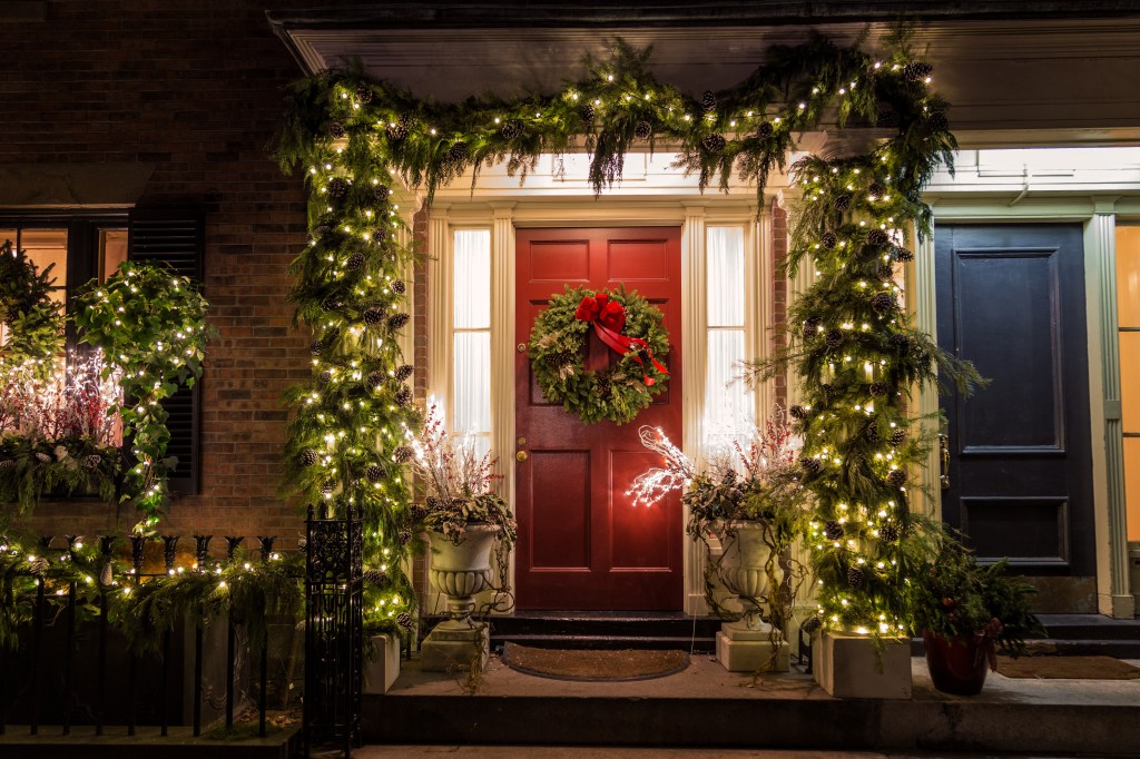 A red door decorated with a festive wreath and twinkling lights